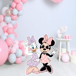 Può includere: Sagome di Daisy Duck e Minnie Mouse in abiti e occhiali da sole, con un arco di palloncini rosa e altre decorazioni per feste. I personaggi sono in un'ambientazione festosa con palloncini rosa, bianchi e azzurri, e un tavolino bianco.