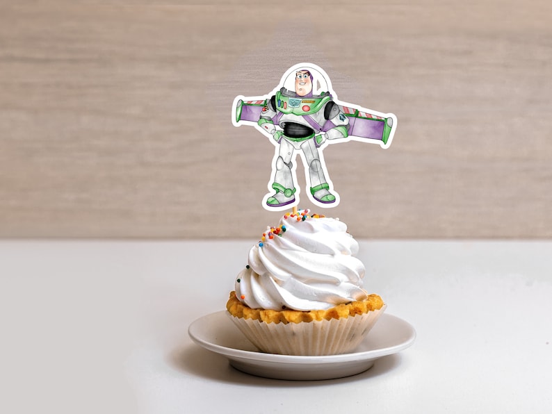 May include: A white cupcake with colorful sprinkles topped with a white frosting swirl. A cartoon image of Buzz Lightyear from the Toy Story movie is on a stick and placed on top of the cupcake.