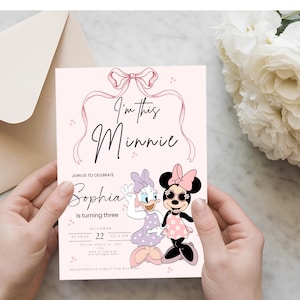 May include: A light pink invitation card with the text "I'm this Minnie" and "Sophia is turning three". The card features illustrations of Minnie Mouse and Daisy Duck. A light pink envelope and white flowers are in the background.