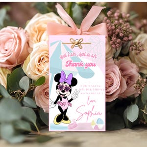 Może przedstawiać: Różowa etykieta prezentowa z ilustracją Myszki Minnie, napisami "splash, splash, Thank you" i "For making my birthday so magical! Love, Sophia". Etykieta jest zawiązana różową wstążką, na tle róż.