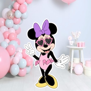 May include: A cartoon cutout of Minnie Mouse wearing heart-shaped sunglasses, a pink dress, and a purple bow. She is giving a peace sign. The background includes pink, white, and silver balloons, and a small white table with decorations.