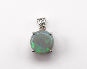 Op de afbeelding: Een zilveren hanger met een ronde, donkergrijze opaal met groene en blauwe schittering. De opaal is gezet in een zilveren bezel met vier klauwen.
