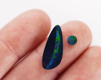 Op de afbeelding: Twee zwarte opalen, een ovale en een ronde, met groene en blauwe iriserende flitsen.