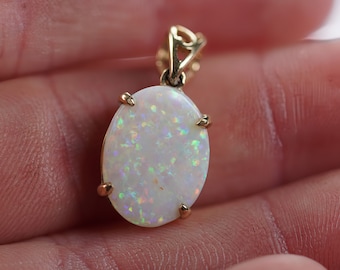 Op de afbeelding: Een gouden hanger met een witte opaal edelsteen met iriserende regenboogflitsen. De opaal is gezet in een ovale gouden zetting met vier grijpklauwen.