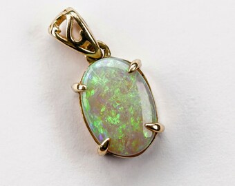 Op de afbeelding: Een gouden hanger met een ovale opaal edelsteen. De opaal heeft een witte basis met groene en blauwe iriserende flitsen.