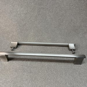 May include: Two brushed nickel cabinet pulls with a rectangular design. Each pull has a straight bar and square end pieces. The pulls are shown on a gray background.