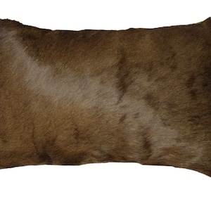 May include: A brown cowhide pillow with a soft, fuzzy texture. The pillow is rectangular and has a slightly rounded shape.