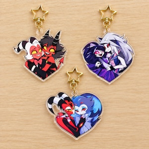 Può includere: Tre portachiavi in acrilico a forma di cuore con coppie di personaggi dei cartoni animati. Ogni ciondolo ha una chiusura dorata a forma di stella. I disegni raffigurano Moxxie e Millie, Octavia e Loona, e Blitzo e Stolas in colori vivaci.