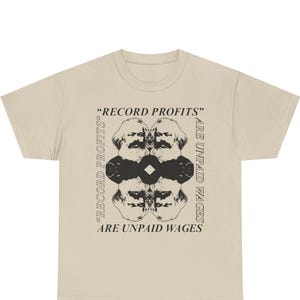 May include: A beige t-shirt with a black graphic. The design includes a mirrored face and the text "RECORD PROFITS" and "ARE UNPAID WAGES".