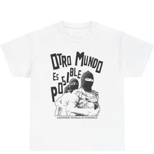 May include: White t-shirt with a black and white graphic. The graphic features two figures wearing balaclavas, with the words "OTRO MUNDO ES POSIBLE" and "ANOTHER WORLD IS POSSIBLE" printed above and below the figures.