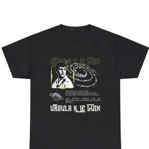 以下が含まれることがあります： 白いグラフィックが施された黒いTシャツ。有名なSF作家であるアーシュラ・K・ル・グインの画像と、人間の力についての引用が書かれています。グラフィックには、銀河のスタイリッシュな画像も含まれています。