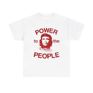 May include: A white short-sleeved t-shirt featuring a red graphic print of a person wearing a beret in the centre. The text "POWER to the PEOPLE" is printed in red capital letters, with "POWER" arched above the portrait and "PEOPLE" below.