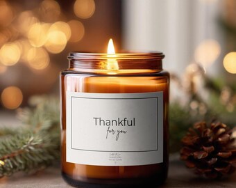 Könnte beinhalten: Eine brennende Kerze in einem bernsteinfarbenen Glasgefäß mit einem weißen rechteckigen Etikett. Das Etikett hat einen dünnen schwarzen Rand und den Text Thankful for you in einer schwarzen Serifenschrift und Schreibschrift. Das Wachs ist goldfarben.
