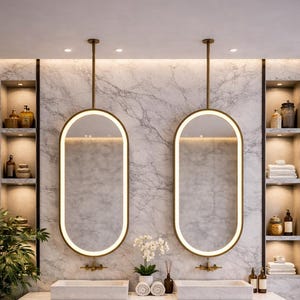 Può includere: Un moderno design di bagno con due specchi ovali illuminati con cornici dorate sospesi sopra lavandini rettangolari. Il mobile ha una base in legno scuro e un piano in marmo. Mensole su entrambi i lati espongono oggetti decorativi.