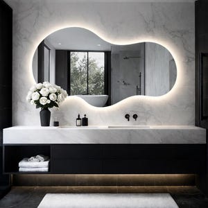 May include: A modern bathroom vanity with a large, organically shaped mirror with integrated lighting. The vanity features a white marble countertop, black cabinets, and a black vase with white roses. The overall design is minimalist and luxurious.