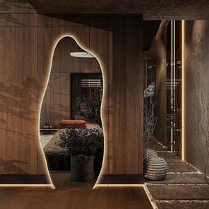 Peut inclure: Intérieur moderne d'un couloir avec des panneaux de bois et un grand miroir de forme organique avec un contour lumineux et chaleureux. L'espace comprend un chemin en pierre, des plantes en pot et un éclairage ambiant, créant une atmosphère sereine.