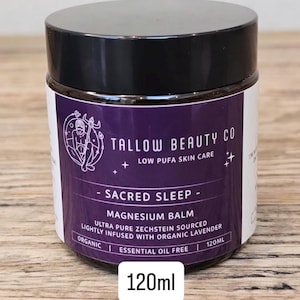 Puede incluir: Un tarro de 120ml de b&aacute;lsamo de magnesio Sacred Sleep de Tallow Beauty Co. con tapa negra y etiqueta morada. La etiqueta presenta un gr&aacute;fico circular y el texto "Low Pufa Skin Care", "Ultra Pure Zechstein Sourced" y "Lightly Infused With Organic Lavender".
