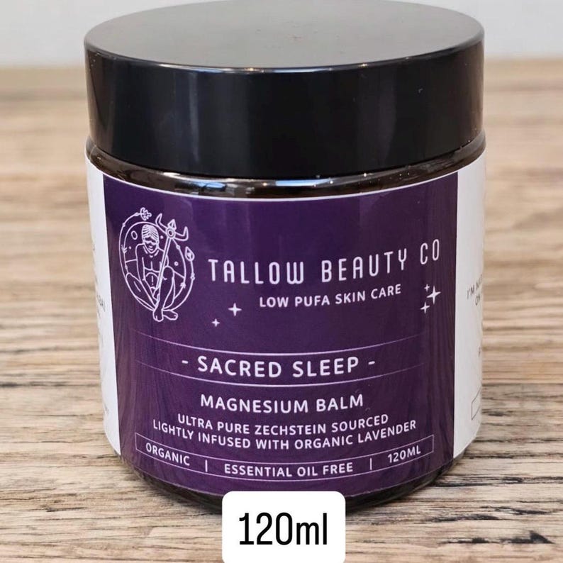 Puede incluir: Un tarro de 120ml de b&aacute;lsamo de magnesio Sacred Sleep de Tallow Beauty Co. con tapa negra y etiqueta morada. La etiqueta presenta un gr&aacute;fico circular y el texto "Low Pufa Skin Care", "Ultra Pure Zechstein Sourced" y "Lightly Infused With Organic Lavender".