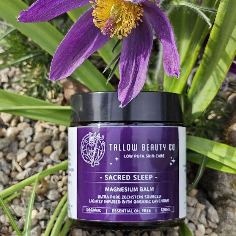 Puede incluir: Un tarro negro de b&aacute;lsamo de magnesio Sacred Sleep de Tallow Beauty Co. con una etiqueta morada. La etiqueta presenta un logotipo circular y el texto "Low Pufa Skin Care", "Sacred Sleep", "Magnesium Balm" y "Ultra Pure Zechstein Sourced", 120ml.