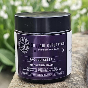 May include: A jar of Tallow Beauty Co. Sacred Sleep Magnesium Balm. The jar has a black lid and a purple label with white text. The label includes the text "Ultra Pure Zechstein Sourced" and "Lightly infused with organic lavender". The jar contains 120ml.