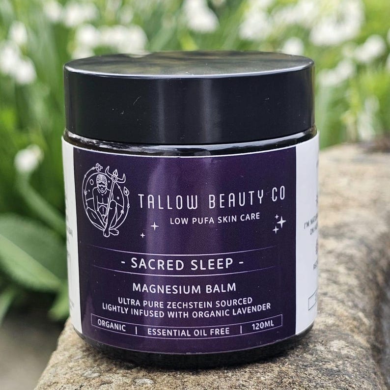Puede incluir: Un frasco oscuro con tapa negra que contiene b&aacute;lsamo de magnesio Sacred Sleep de Tallow Beauty Co. La etiqueta morada presenta texto blanco que indica 120ml, org&aacute;nico, sin aceites esenciales y fuente Zechstein pura, con un gr&aacute;fico de una persona.