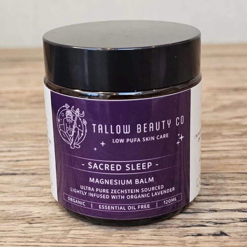 Puede incluir: Un tarro de 120ml de b&aacute;lsamo de magnesio Sacred Sleep de Tallow Beauty Co. con tapa negra y etiqueta morada. La etiqueta presenta una ilustraci&oacute;n de l&iacute;nea blanca de una figura, el texto Low Pufa Skin Care, y notas de que es org&aacute;nico y sin aceites esenciales.