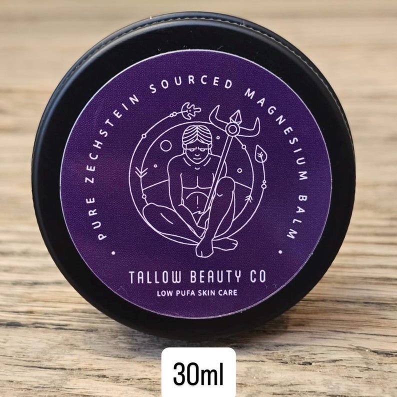 Puede incluir: Un recipiente negro redondo de b&aacute;lsamo de magnesio Tallow Beauty Co. con una etiqueta morada. La etiqueta presenta un dibujo lineal blanco de una figura sosteniendo un tridente, rodeado por el texto Pure Zechstein Sourced Magnesium Balm, 30ml.