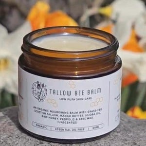 May include: A brown glass jar with a white label that reads "Tallow Bee Balm Low PUFA Skin Care". The label also includes a list of ingredients, including Scottish Tallow, Mango Butter, Jojoba Oil, Raw Honey, Propolis & Bees Wax. The jar is sitting on a grey surface.