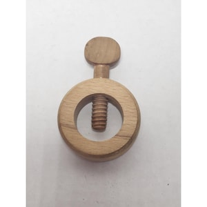 May include: A wooden nutcracker with a circular body and a threaded screw mechanism. The nutcracker has a small, round handle at the top and is made of light-colored wood.