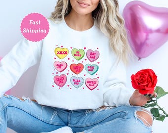 May include: White sweatshirt with a Valentine's Day theme featuring colorful candy hearts with phrases like "XOXO", "Be Mind", "Say Yes", "Kiss Me", "Hug Me", "Best Day", "Text Me", "Miss You", and "Sweet Talk".