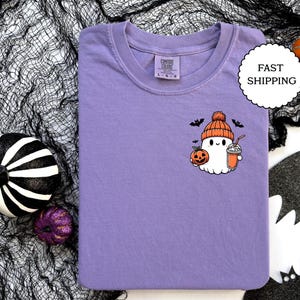 Pu&ograve; includere: Maglietta viola con un simpatico fantasma dei cartoni animati che indossa un cappello a forma di zucca e tiene una zucca e una bevanda. Il fantasma indossa un cappello marrone con un pon pon bianco. Il fantasma sorride e ha un'espressione amichevole. La maglietta &egrave; un ottimo regalo per Halloween.