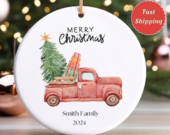 May include: White ceramic Christmas ornament with a red vintage truck carrying a Christmas tree and gifts. The ornament has the words "Merry Christmas" and "Smith Family 2024" printed on it.