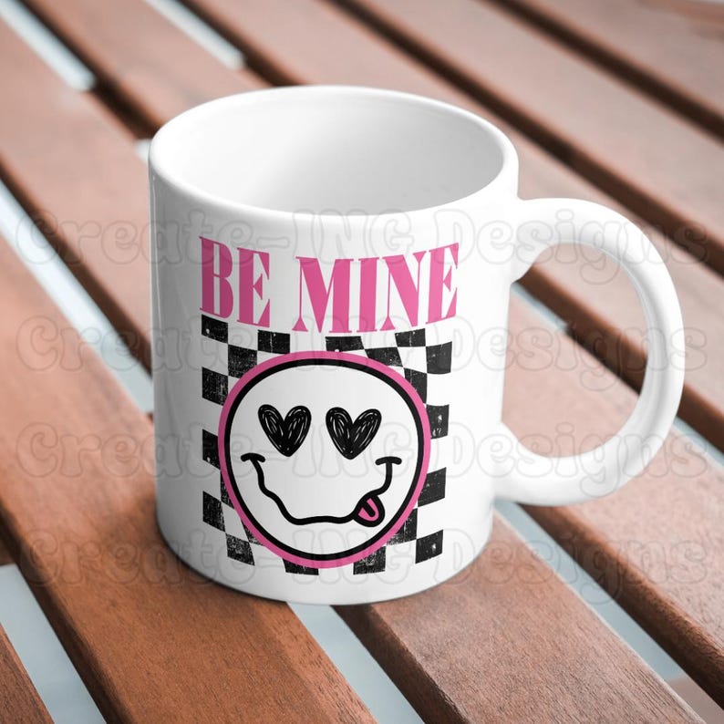 May include: White ceramic mug with a black and white checkered pattern and a pink smiley face with hearts for eyes. The text "BE MINE" is printed in pink on the mug.