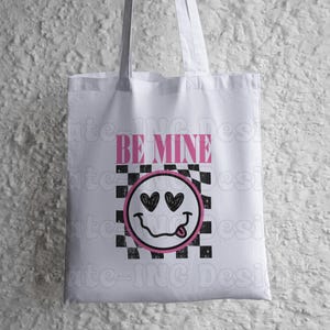 May include: White tote bag with a black and white checkered pattern and a pink smiley face with hearts for eyes. The text "BE MINE" is printed in pink above the smiley face.