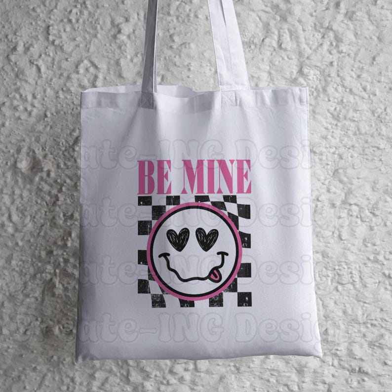 May include: White tote bag with a black and white checkered pattern and a pink smiley face with hearts for eyes. The text "BE MINE" is printed in pink above the smiley face.