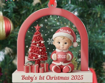 May include: A Christmas ornament featuring a baby in a Santa suit holding a heart-shaped object with "2025" on it. The ornament has a red arch, a Christmas tree, and the text "Baby's 1st Christmas 2025".
