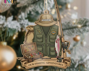 May include: Wooden Christmas ornament featuring fishing gear, including a vest, hat with "ANDREW" on it, fishing rod, and a trout. A banner reads "OUR FISHING ADVENTURES". A tackle box and a sack are also included.
