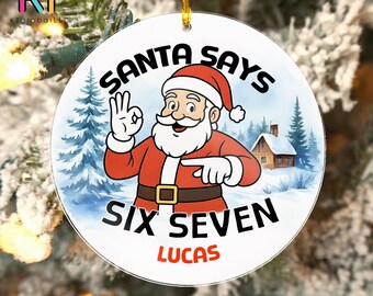 May include: Round Christmas ornament featuring Santa Claus in a red suit and hat, with the text "SANTA SAYS SIX SEVEN LUCAS". The ornament has a winter scene background with snow, trees, and a house.