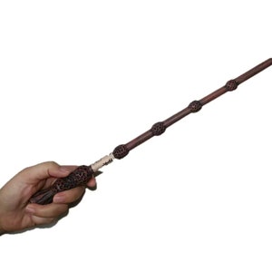 May include: A brown wooden wand with a dark brown handle and a black tip. The wand is decorated with a series of small, round, black knobs.