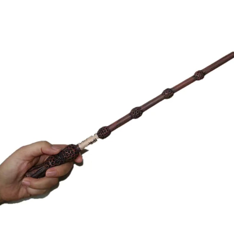 May include: A brown wooden wand with a dark brown handle and a black tip. The wand is decorated with a series of small, round, black knobs.