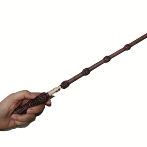 May include: A dark brown wooden wand with three silver accents. The wand is approximately 13 inches long.