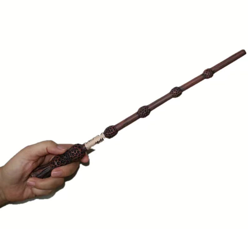 May include: A dark brown wooden wand with three silver accents. The wand is approximately 13 inches long.