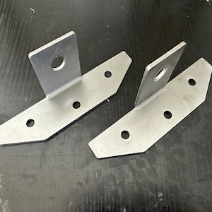 May include: Two silver metal brackets with four holes each and a larger hole in the center of the upright section. The brackets are designed for mounting.