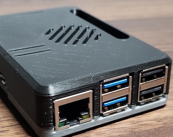 Op de afbeelding: Een donkergrijze rechthoekige elektronische behuizing met ventilatiesleuven en meerdere USB-poorten. De behuizing heeft een gestructureerd oppervlak en is ontworpen om elektronische componenten te huisvesten. De poorten hebben blauwe en zilveren accenten.