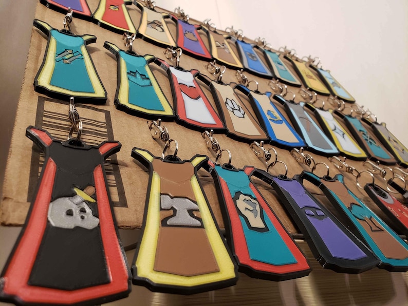 May include: A collection of colorful, printed keychains shaped like aprons. Each keychain features a different design, including a skull, a hammer, a fist, and a paw print. The keychains are made of a durable plastic material and are perfect for adding a touch of personality to your keys.