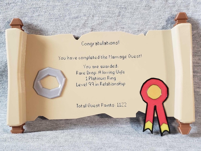 Op de afbeelding: Decoratieve scroll-vormige plaquette met de tekst "Gefeliciteerd! Je hebt de Huwelijksquest voltooid!" en andere tekst. Het heeft een zilveren ring en een rood lint met gele accenten. De plaquette is beige met bruine accenten.