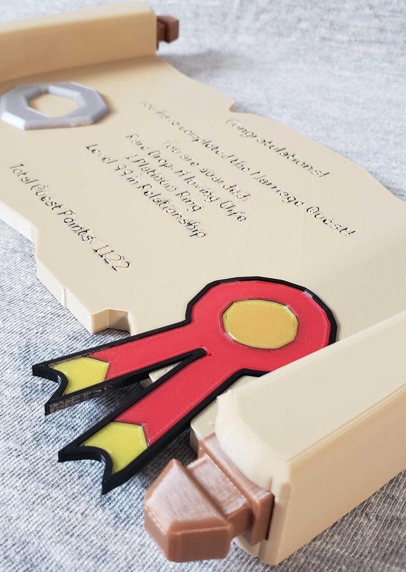 Op de afbeelding: Een beige, scroll-vormige plaat met zwarte tekst, een rood en geel lint en een zilveren ring. De tekst luidt "Gefeliciteerd! Je hebt de Huwelijksquest voltooid!" en andere details over een relatie.