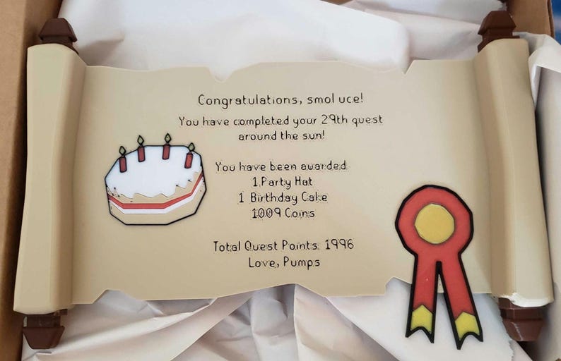 Op de afbeelding: Een decoratieve rol met tekst en illustraties. De tekst luidt "Gefeliciteerd, smol uce! Je hebt je 29e zoektocht rond de zon voltooid!" en somt beloningen op. Bevat een verjaardagstaart en een rood lint.