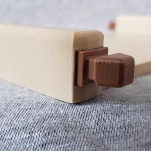 Op de afbeelding: Een lichtbeige houten meubelcomponent met een donkerbruin, vierkant accent. De component is rechthoekig met een uitstekend vierkant element. De achtergrond is een grijze stof.