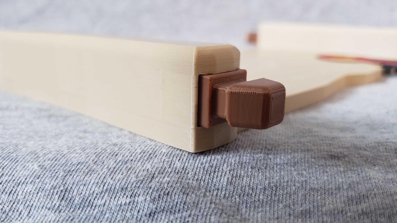 Op de afbeelding: Een lichtbeige houten meubelcomponent met een donkerbruin, vierkant accent. De component is rechthoekig met een uitstekend vierkant element. De achtergrond is een grijze stof.